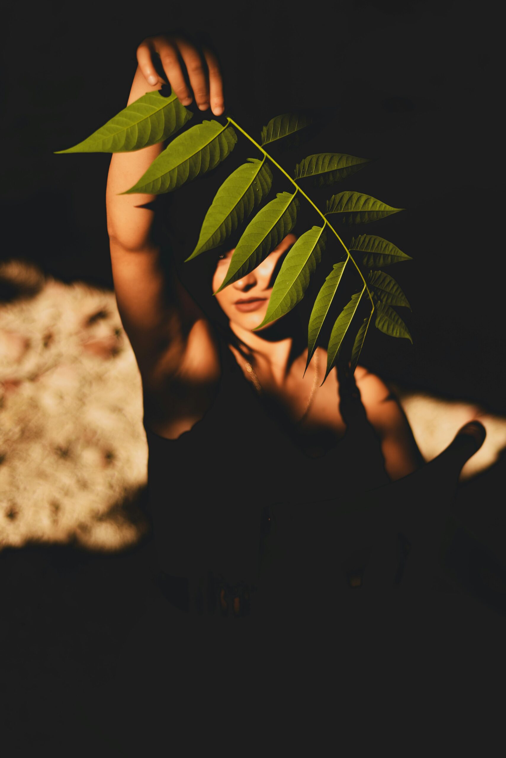 A captivating portrait of a woman partially covered by a leaf under golden sunlight.